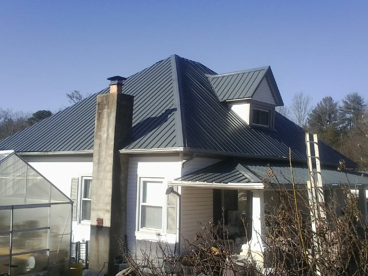 Dark blue standing seam metal roof on a white farmhouse with dormer — Slate & Tile Roof Repair by Roofing Brothers in Moro