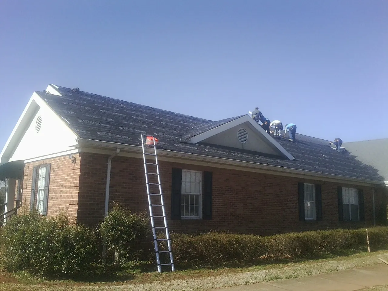 Crew tearing shingles off a brick ranch roof with a ladder set — Metal Roof Repair work by our crew in Moro