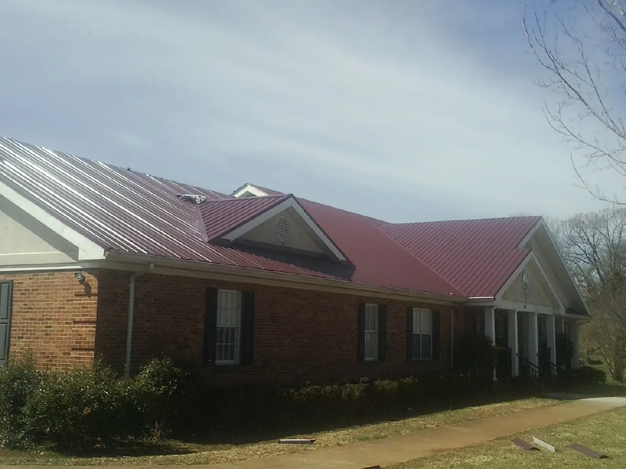 Red metal roof with gabled entries on a long brick building, from a Hail Damage Roof Repair job in Moro