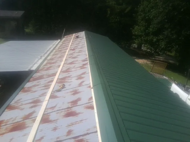 Old rusted panels beside newly installed green metal roofing — Wind Damage Roof Repair by Roofing Brothers in Moro