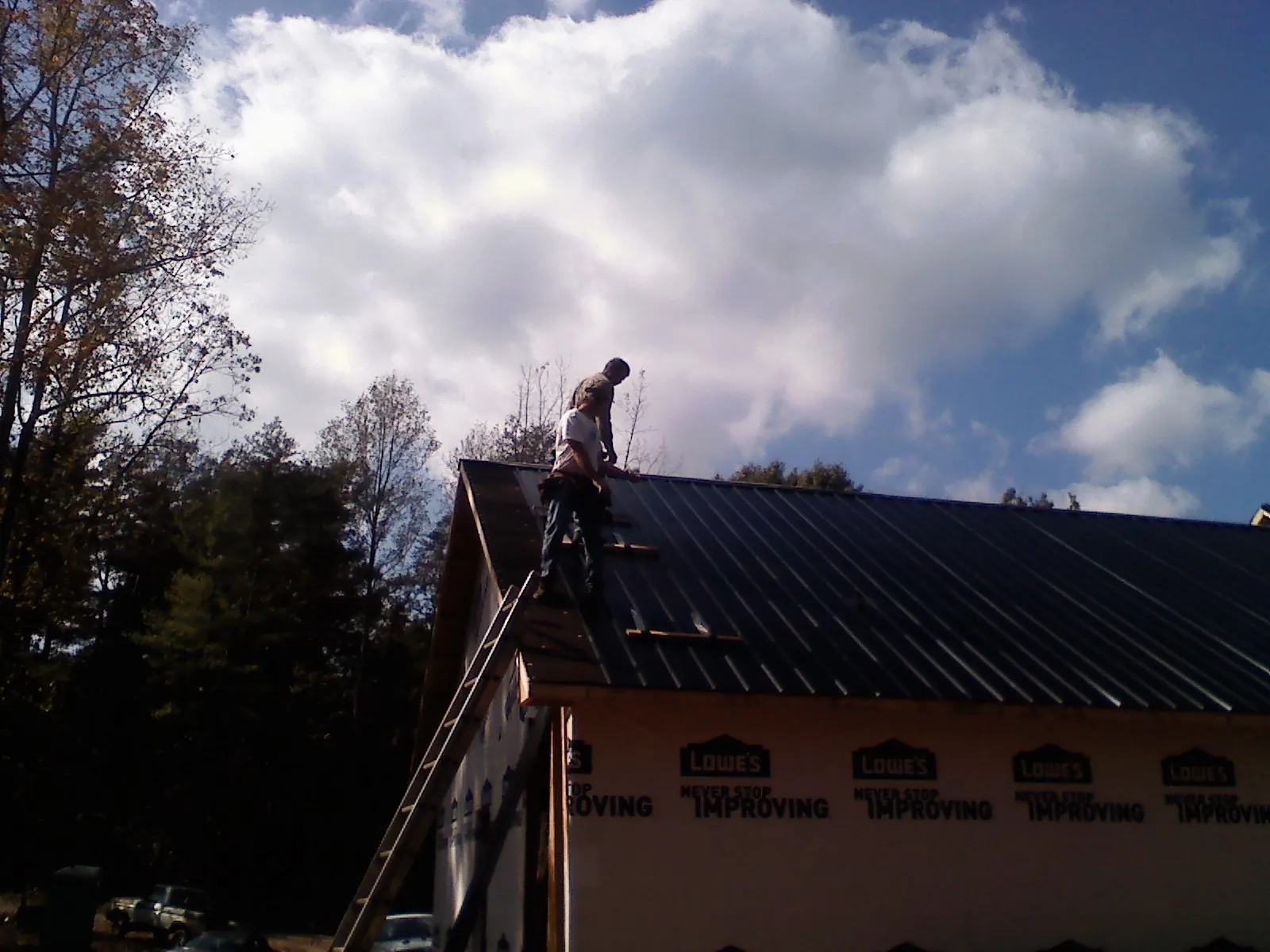 Roofer fastening dark metal panels high against a cloudy sky, from a Roof Inspection job in Moro